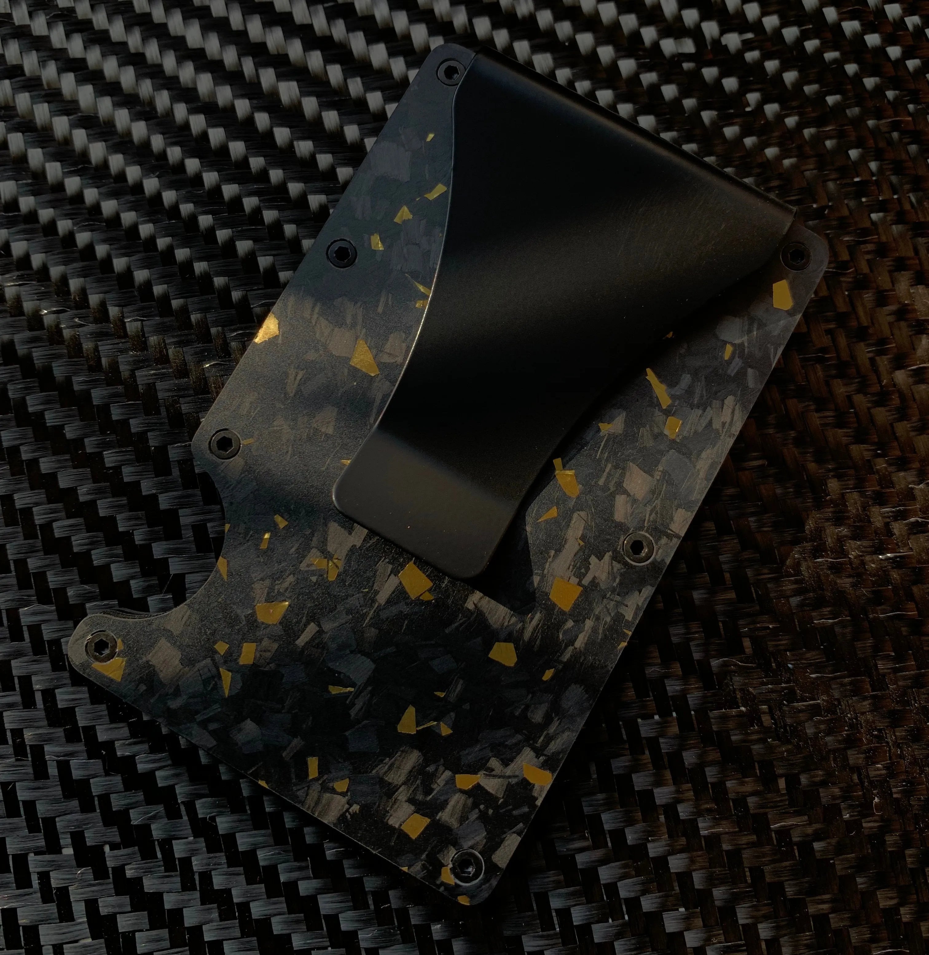 Black and gold patterned wallet on a carbon fiber background